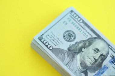 Büyük miktarlarda 100 dolarlık banknotlar parlak sarı renkli kağıtların üzerinde uzanır.