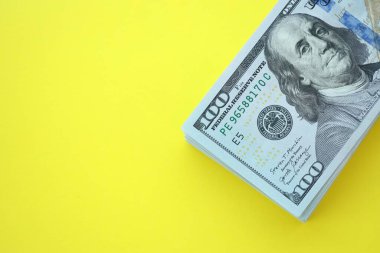 Büyük miktarlarda 100 dolarlık banknotlar parlak sarı renkli kağıtların üzerinde uzanır.