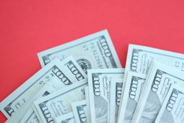 Büyük miktarlarda 100 dolarlık banknotlar parlak kırmızı kağıtların üzerinde duruyor.