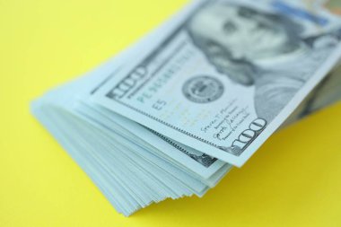 Büyük miktarlarda 100 dolarlık banknotlar parlak sarı renkli kağıtların üzerinde uzanır.