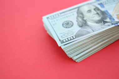Büyük miktarlarda 100 dolarlık banknotlar parlak kırmızı kağıtların üzerinde duruyor.
