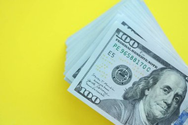 Büyük miktarlarda 100 dolarlık banknotlar parlak sarı renkli kağıtların üzerinde uzanır.