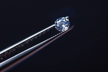 Metal kuyumcu cımbızında tutulan elmas seçici odaklı, yakın mesafeden kesilmiş parlak taş. Profesyonel fotoğraf.