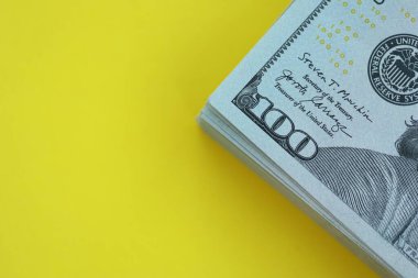 Büyük miktarlarda 100 dolarlık banknotlar parlak sarı renkli kağıtların üzerinde uzanır.