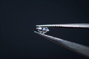Metal kuyumcu cımbızında tutulan elmas seçici odaklı, yakın mesafeden kesilmiş parlak taş. Profesyonel fotoğraf.