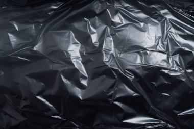 Siyah buruşmuş plastik filmin işlenmiş görüntüsü, koyu bir arkaplanda gölgeler.