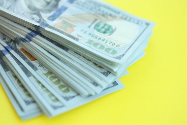 Büyük miktarlarda 100 dolarlık banknotlar parlak sarı renkli kağıtların üzerinde uzanır.