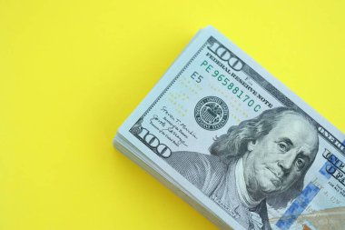 Büyük miktarlarda 100 dolarlık banknotlar parlak sarı renkli kağıtların üzerinde uzanır.