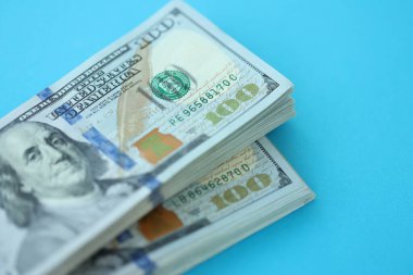 Büyük miktarlarda 100 dolarlık banknotlar parlak mavi renkli kağıtların üzerinde uzanır.