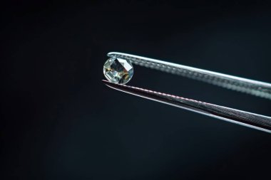 Metal kuyumcu cımbızında tutulan elmas seçici odaklı, yakın mesafeden kesilmiş parlak taş. Profesyonel fotoğraf.