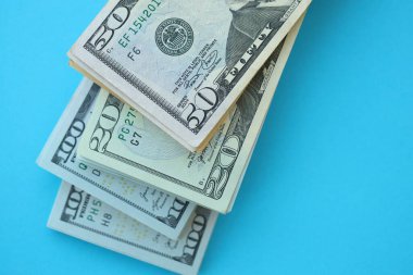 Büyük miktarda yüz, elli ve yirmi dolarlık banknotlar parlak mavi renkli kağıtların üzerinde uzanır.