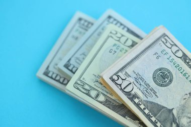 Büyük miktarda yüz, elli ve yirmi dolarlık banknotlar parlak mavi renkli kağıtların üzerinde uzanır.