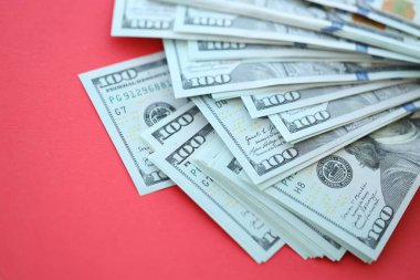Büyük miktarlarda 100 dolarlık banknotlar parlak kırmızı kağıtların üzerinde duruyor.