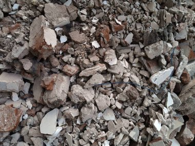 Kırık kırmızı tuğlalar ve beton parçaları. Yıkılmış bir binanın enkazı. İnşaat alanında büyük beton ve taş atığı var.