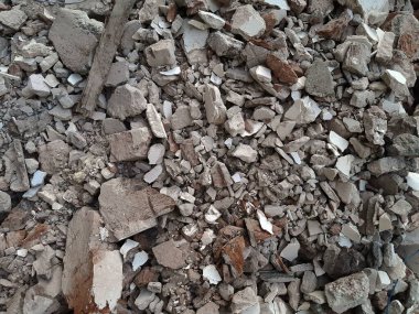 Kırık kırmızı tuğlalar ve beton parçaları. Yıkılmış bir binanın enkazı. İnşaat alanında büyük beton ve taş atığı var.