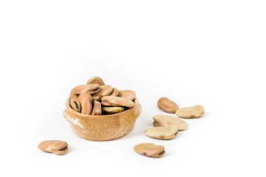 Fava fasulyeleri beyaz üzerine izole edilmiş seramik bir kasenin etrafına saçılmış.