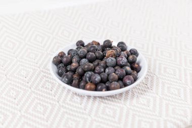 Dried juniper berries in a white bowl over fabric