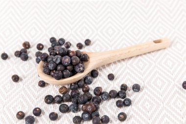 Dried juniper berries scattered around a wood spoon over fabric top down