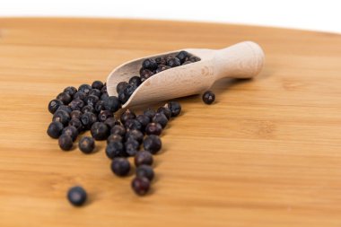 Dried juniper berries scattered around a wood scoop over wood board side view