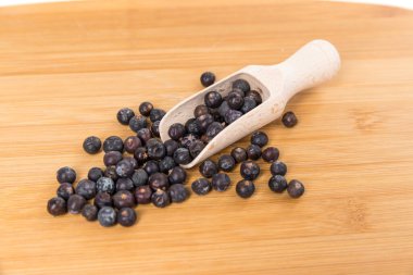 Dried juniper berries spilling out of wood scoop on cutting board top down