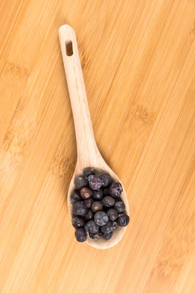 Dried juniper berries in a wood spoon over wood board top down