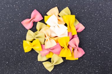 Çok renkli yeşil sarı ve kırmızı papyonlu makarna yığını siyah kesim tahtasının tepesinde