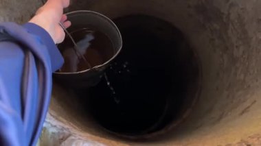 Parlak, güneşli bir günde, bir insan eli tarafından ahşap bir kuyudan metal bir kova çıkarılır. Onu kaldırdıktan sonra, su kuyuya geri dökülüyor. Video, el ve kovaya odaklanıyor. Doğal ışıkla huzurlu bir kırsal anı yakalıyor.