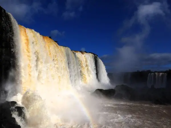 Iguazu Nehri ve arka planda güzel bir gökkuşağı ile şelale.