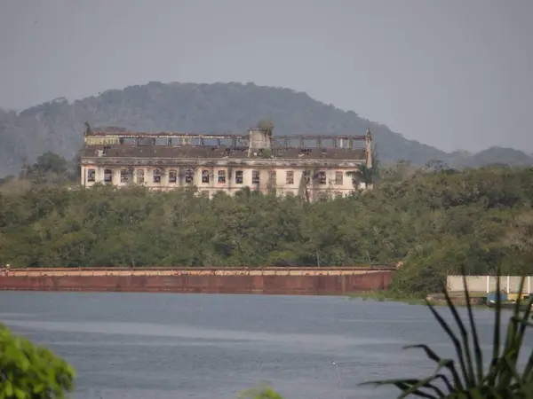 Sakin sulara bakan harap bir yapı, doğa tarafından ele geçirilmiş. Unutulmuş bir tarihi ve çürümeyi çağrıştırıyor..