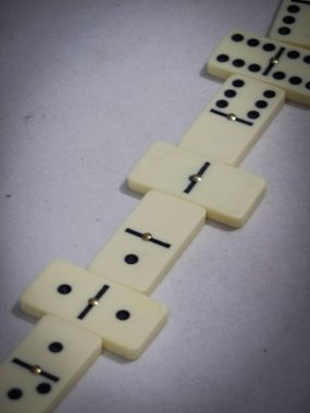 Yakın çekim, zincirleme reaksiyona girmeye hazır gibi duran domino taşlarını yakalar. Tarafsız arka plan dominoların dokulu yüzeyini vurgular..