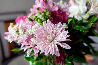 Pembe kasımpatı, beyaz zambaklar, güller, asterlar ve diğer mevsimlik çiçeklerden oluşan canlı bir çiçek buketi. Romantik, ilkbahar veya kutlama temaları için mükemmel. Kapalı alanda doğal ışıkta yakalandılar..