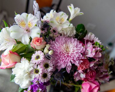 Pembe kasımpatı, beyaz zambaklar, güller, asterlar ve diğer mevsimlik çiçeklerden oluşan canlı bir çiçek buketi. Romantik, ilkbahar veya kutlama temaları için mükemmel. Kapalı alanda doğal ışıkta yakalandılar..