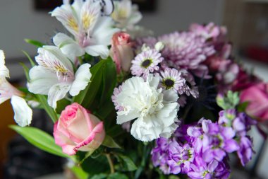 Pembe kasımpatı, beyaz zambaklar, güller, asterlar ve diğer mevsimlik çiçeklerden oluşan canlı bir çiçek buketi. Romantik, ilkbahar veya kutlama temaları için mükemmel. Kapalı alanda doğal ışıkta yakalandılar..