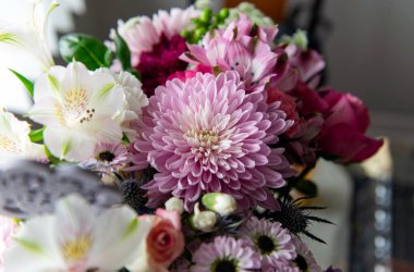 Pembe kasımpatı, beyaz zambaklar, güller, asterlar ve diğer mevsimlik çiçeklerden oluşan canlı bir çiçek buketi. Romantik, ilkbahar veya kutlama temaları için mükemmel. Kapalı alanda doğal ışıkta yakalandılar..