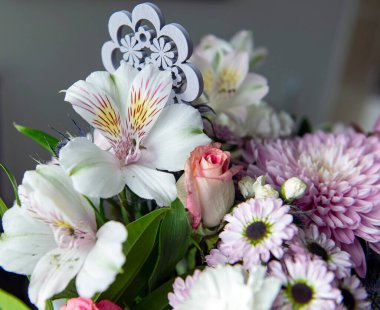 Pembe kasımpatı, beyaz zambaklar, güller, asterlar ve diğer mevsimlik çiçeklerden oluşan canlı bir çiçek buketi. Romantik, ilkbahar veya kutlama temaları için mükemmel. Kapalı alanda doğal ışıkta yakalandılar..