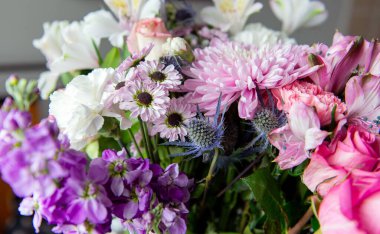 Pembe kasımpatı, beyaz zambaklar, güller, asterlar ve diğer mevsimlik çiçeklerden oluşan canlı bir çiçek buketi. Romantik, ilkbahar veya kutlama temaları için mükemmel. Kapalı alanda doğal ışıkta yakalandılar..