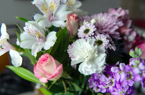 Pembe kasımpatı, beyaz zambaklar, güller, asterlar ve diğer mevsimlik çiçeklerden oluşan canlı bir çiçek buketi. Romantik, ilkbahar veya kutlama temaları için mükemmel. Kapalı alanda doğal ışıkta yakalandılar..