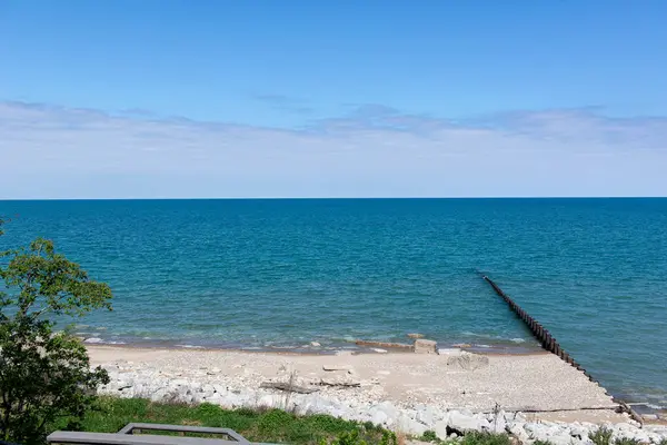 Sakin bir göl manzarası berrak mavi su, kayalık bir plaj ve ufka doğru uzanan uzun bir iskele. Güneşli bir günde hafif bulutlar ve sakin dalgalarla yakalandılar. Seyahat, rahatlama veya doğayla ilgili konular için ideal.