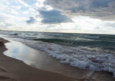 Tepesinde dramatik bulutlar olan dinamik dalgalar sahile yuvarlanıyor. Michigan Gölü kıyı şeridinin doğal manzarası, doğa, seyahat ve arka plan temaları için mükemmel.