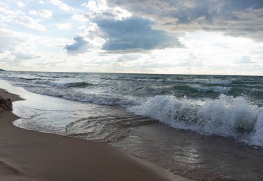 Tepesinde dramatik bulutlar olan dinamik dalgalar sahile yuvarlanıyor. Michigan Gölü kıyı şeridinin doğal manzarası, doğa, seyahat ve arka plan temaları için mükemmel.