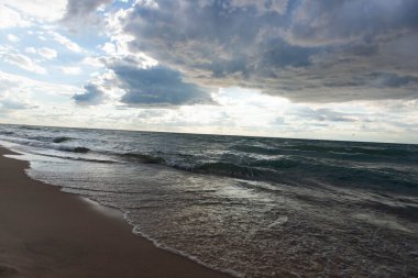 Michigan Gölü kıyıları yumuşak dalgalı ve nemli kumla kaplı. Karamsar gökyüzü ve manzaralı manzara sakin ve doğal bir kıyı arkaplanı yaratır.