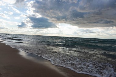 Michigan Gölü kıyıları yumuşak dalgalı ve nemli kumla kaplı. Karamsar gökyüzü ve manzaralı manzara sakin ve doğal bir kıyı arkaplanı yaratır.