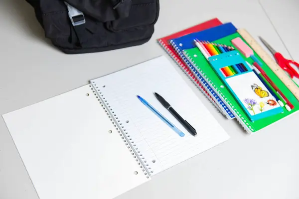 Boş sayfaları ve iki kalemi olan spiral bir defter aç. Kalem, cetvel, silgi ve makas da dahil olmak üzere rengarenk okul malzemeleri. Eğitim, ödev ve öğrenim kavramı.
