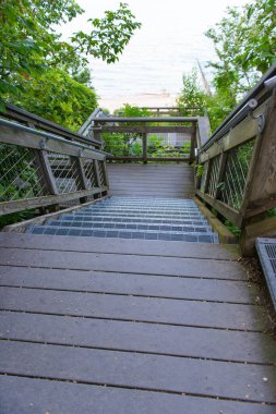 Verimli yeşil ağaçların arasından Michigan Gölü 'nün kumlu ve mavi sularına doğru inen metal basamaklı ahşap merdivenlerin manzarası, yaz manzarası..