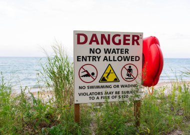 Uyarı işareti ve kırmızı can simidi kıyıya yerleştirildi. Arka planda doğal peyzaj bulunan yüzme ya da suya girme yasağı uyarısı.
