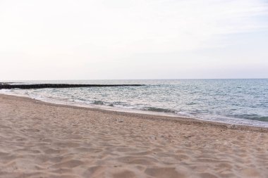 Yumuşak deniz dalgaları ve ufukta dalgalar olan huzurlu kumlu bir sahil. Seyahat, tatil ve doğa geçmişi için ideal sakin kıyı manzarası.