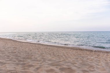 Sakin deniz dalgaları temiz ufuk ve pastel gökyüzü ile kumlu sahili yıkıyor. Arka plan, tasarım veya seyahat konsepti için minimalist kıyı manzarası.