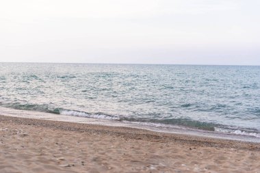 Sakin deniz dalgaları temiz ufuk ve pastel gökyüzü ile kumlu sahili yıkıyor. Arka plan, tasarım veya seyahat konsepti için minimalist kıyı manzarası.