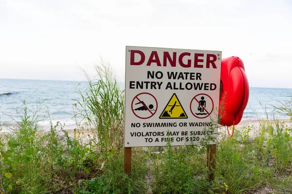 Uyarı işareti ve kırmızı can simidi kıyıya yerleştirildi. Arka planda doğal peyzaj bulunan yüzme ya da suya girme yasağı uyarısı.