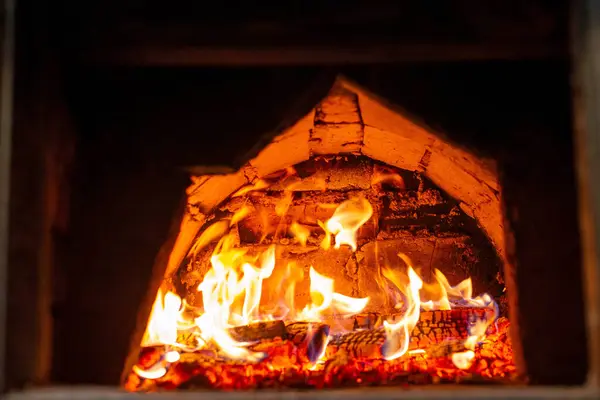 Parlak odun ve içinde ev yapımı ekmek pişirme ve geleneksel yemek pişirme için kullanılan parlak alevlerle taşralı bir tuğla fırını kapatın..